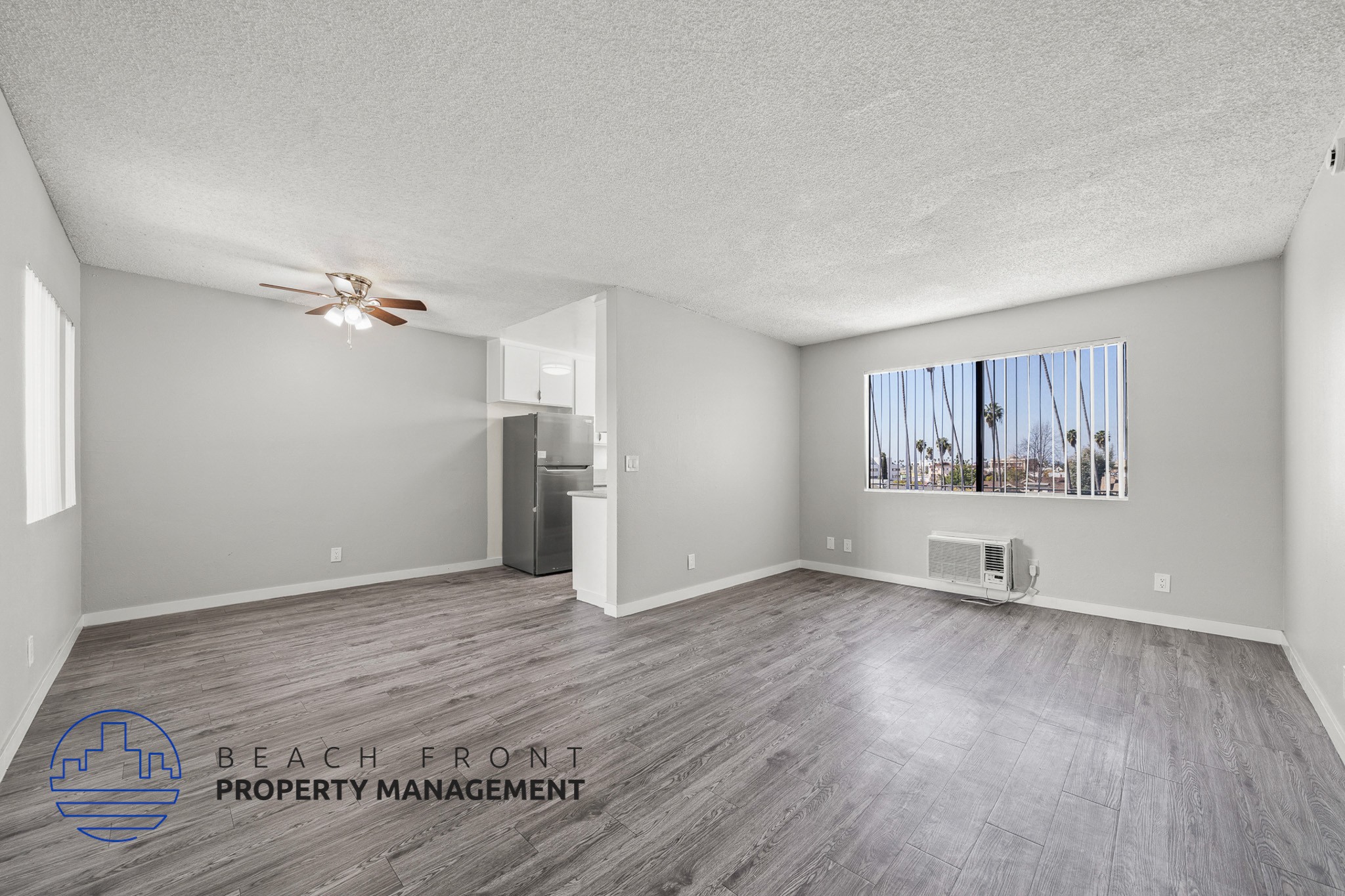 A spacious room with a ceiling fan and a window overlooking a beach.